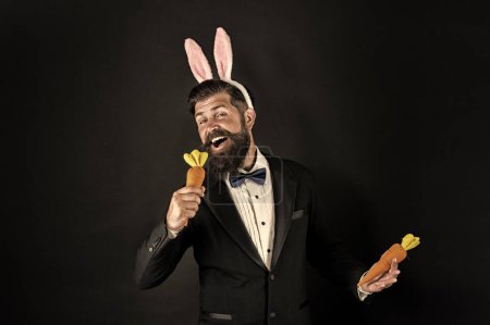 Foto de Siente la canción. Cantante de Pascua. El hombre de negocios finge cantar con zanahoria. El barbudo canta la canción fondo negro. Disfrutando de la canción de Pascua. Canción de karaoke. Concierto de música. Humor y melodía. Como música para mis oídos. - Imagen libre de derechos