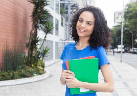 Photo for Beautiful caribbean student with books in the city with street and modern buildings in the background - Royalty Free Image