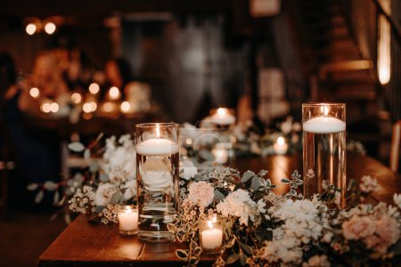 Hermosa decoración de mesa de invitados de boda rústica de lujo mesas de madera con frascos de vidrio y velas, rosas blancas y hojas de eucaypto piezas centrales sobre fondo oscuro. Lujo loft boda.