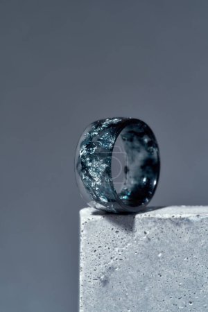 Close up of handmade ring made of dark blue epoxy resin with silver foil inside on concrete element isolated over gray background