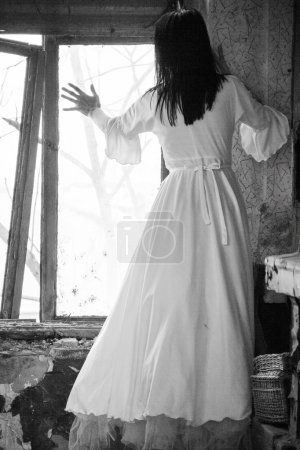 Triste estado de ánimo en una casa vieja y abandonada con una chica que lleva un vestido de novia a la antigua con luz natural. Foto tiene textura de grano visible en su tamaño máximo. Fotografía artística en blanco y negro
