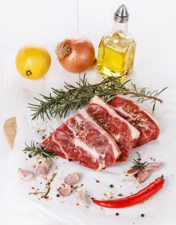 Red meat, vegetables and spices over white background