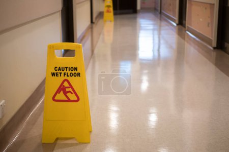 Schild warnt vor nassem Fußboden im Krankenhausflur.