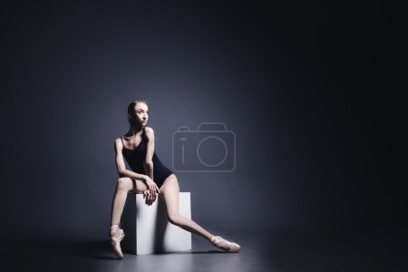 Young ballerina in dark cloth is dancing in a dark of the photostudio