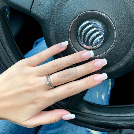 Photo for A graceful female hand with a beautiful manicure lies on the steering wheel - Royalty Free Image
