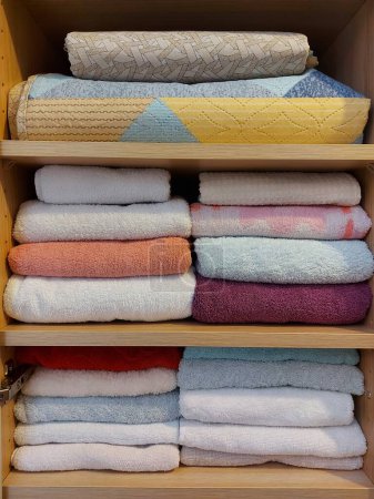 Photo for Multi-colored cotton terry towels stacked neatly on the shelves in the closet. Home textile background - Royalty Free Image