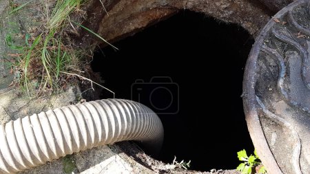 Foto de Una manguera se baja en la alcantarilla para bombear agua fuera de la fosa. limpieza del pozo de alcantarillado. mantenimiento y cuidado en una casa privada - Imagen libre de derechos