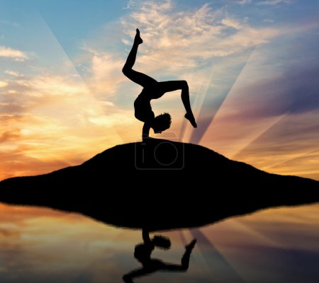 Foto de Concepto de meditación y relajación. Silueta de una chica practicando yoga al atardecer y reflejo en el agua - Imagen libre de derechos