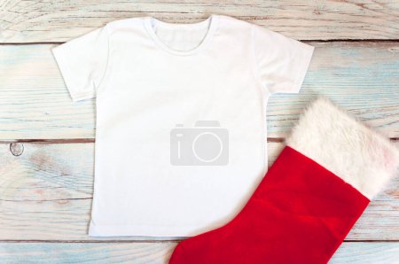 Camisa infantil navideña maqueta - camiseta blanca sobre fondo de madera. Foto de stock.