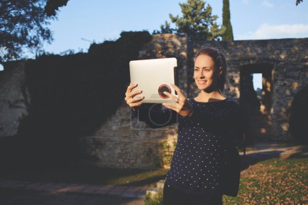  Smiling happy female student is photographing herself with front digital tablet camera