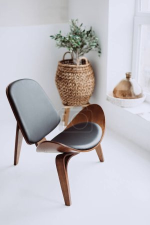 Sillón moderno en cuero negro y madera en un interior de loft blanco. Silla de diseño. Enfoque selectivo suave.