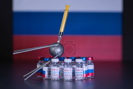 Grupo de vacunas rusas que llevan el nombre de un conocido satélite ruso contra el virus Covid 19 con jeringa. Con la bandera rusa en segundo plano fuera de foco. Texto de la etiqueta lee, inyección de virus corona solamente.