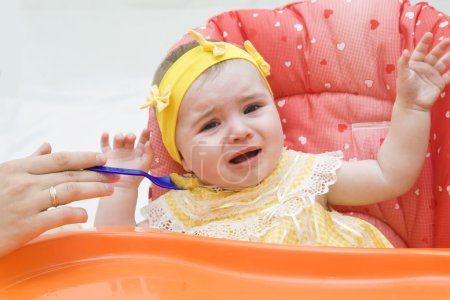 Foto de La niña llorando con comida de cuchara en casa - Imagen libre de derechos