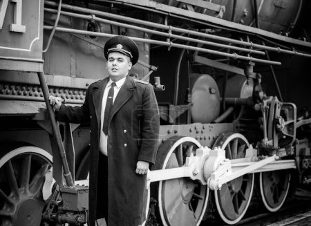Conductor de tren europeo o americano está en su deber en una plataforma y otros trenes. Ferrocarril, trenes de vapor, trenes antiguos