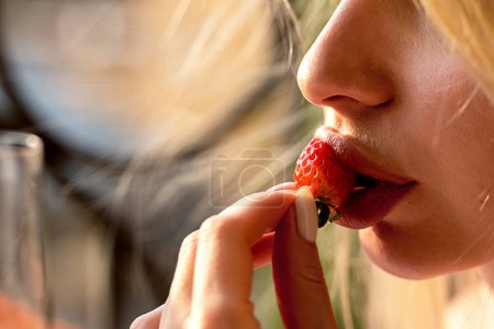 Photo for The girl in a beautiful face eating a berry. Beautiful expressive makeup on the face of the girl. The girl's face close up. Lilac lipstick. The girl in the studio on a white background. - Royalty Free Image