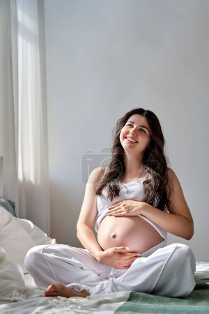 Photo for A beautiful pregnant girl holds her stomach with her hands and smiles. - Royalty Free Image