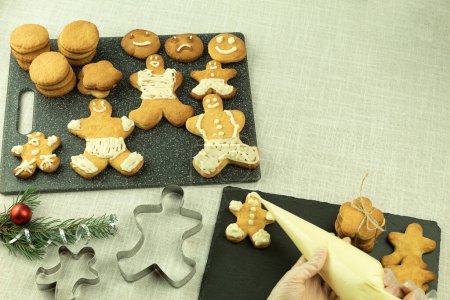 Photo for The girl applies cream to Christmas cookies. Decorating Christmas cookies with a pastry bag. Girl decorates cookies with interest - Royalty Free Image