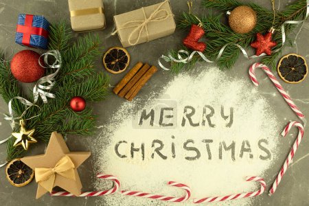 Photo for The inscription on the scattered flour Merry Christmas. Gifts with sweets and Christmas accessories on the table, top view. New year or christmas background with place for text - Royalty Free Image