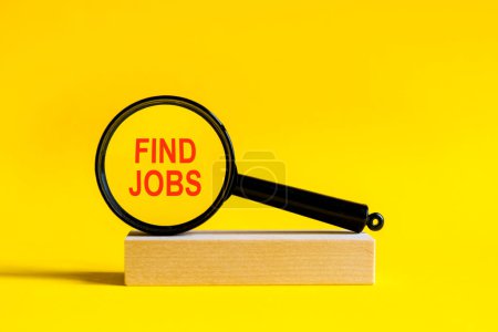 Photo for The inscription find jobs through magnifying glass on yellow background. the magnifying glass is mounted on a wooden stand on a table - Royalty Free Image