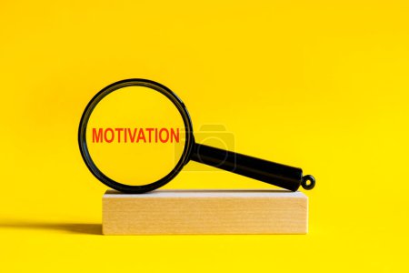 Photo for The inscription Motivation through magnifying glass on yellow background. the magnifying glass is mounted on a wooden stand on a table - Royalty Free Image