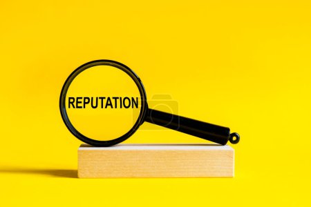 Photo for The inscription Reputation through magnifying glass on yellow background. the magnifying glass is mounted on a wooden stand on a table - Royalty Free Image