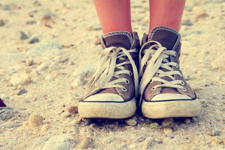 Feet of the child of the teenager in gym shoes on stone track.