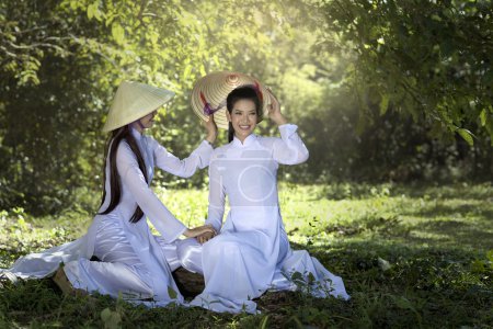 Téléchargez les photos : Deux femmes dans la robe traditionnelle Ao Dai vietnam sous l'arbre - en image libre de droit