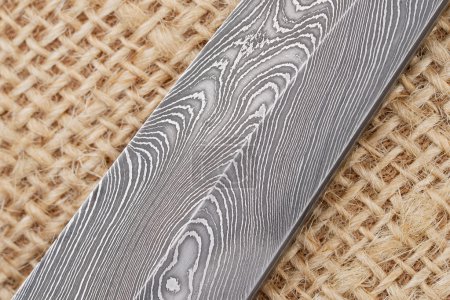 Fragment of the traditional handmade Finnish knife blade with the abstract wave pattern of damascus steel over an old sack background. puzzle 95541086