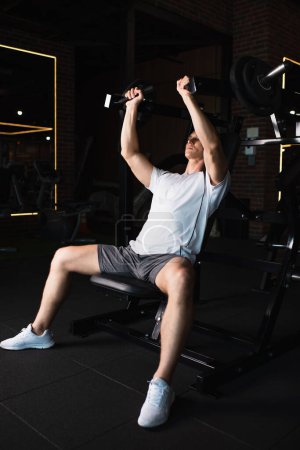 vista completa del hombre en entrenamiento de ropa deportiva en la máquina de ejercicio de extensión de brazo 