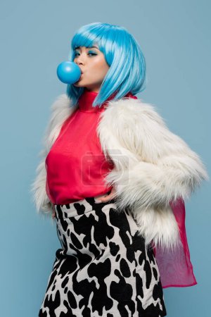 Young asian woman in furry jacket blowing bubble gum isolated on blue 