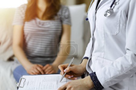 Foto de Primer plano de la mujer-médico y paciente discutiendo el examen de salud actual mientras está sentado en el interior. Permanecer en casa durante la pandemia de Coronavirus y la cuarentena de autoaislamiento. Covid 2019. - Imagen libre de derechos