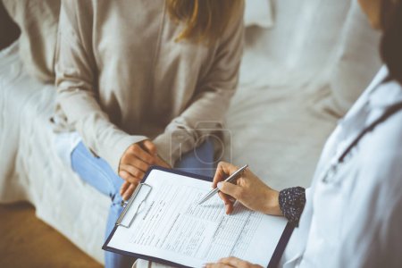 Mujer-médico desconocida y paciente discutiendo el examen de salud actual mientras está sentado en el interior. Permanecer en casa durante la pandemia de Coronavirus y la cuarentena de autoaislamiento