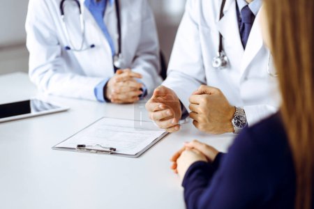 Médico masculino desconocido escuchando a su paciente mujer mientras está sentado en la clínica moderna. Servicio médico perfecto, concepto de medicina durante la pandemia del Coronavirus. Covid 2019