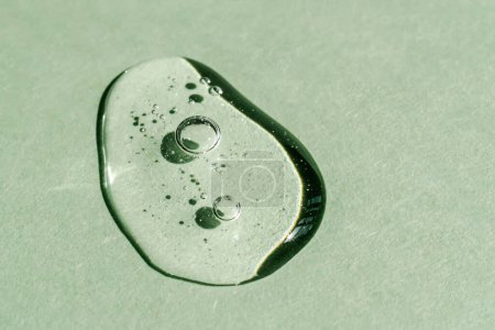 Una gota de gel cosmético transparente sobre un fondo verde.