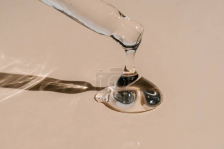 Photo for A drop of cosmetic preparation falls from a pipette on a beige terracotta background . Perfect for showcasing your product. Front view. - Royalty Free Image