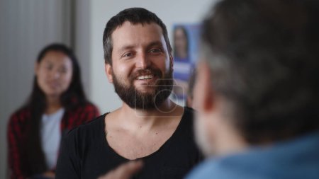 Foto de Hombre adulto encantado contando la historia sobre la superación de la adicción y tomando felicitaciones de los miembros del grupo Alcohólicos Anónimos multirraciales - Imagen libre de derechos