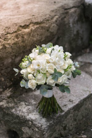 Ramo de boda blanco moderno compuesto de rosas, freesia, lisianto y eucalifo aislados sobre fondo de piedra granulada.