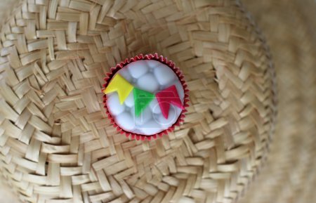 Téléchargez les photos : Cupcake décoré de petits drapeaux colorés pour célébrer St John au Brésil servi sur un chapeau de foin traditionnel - en image libre de droit