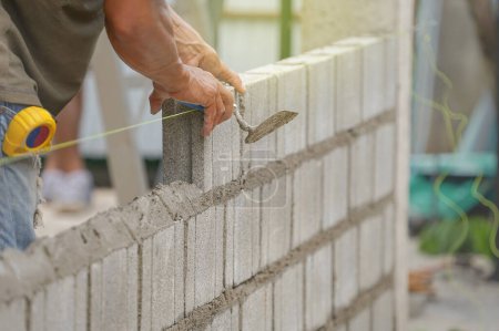 Maurer Hände halten Ziegelkelle aus Aluminium, die Ziegelsteine auf Baustelle installiert, selektiver Fokus                             