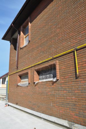 Closeup on Gas Pipe Line System Connection Installed in House Wall and Rain Gutter. Make Gas Line Connections From Steel or Copper Pipes to Ranges, Clothes Dryers Safe and Secure by Using Proper Fittings.