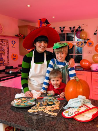 Foto de Madre y dos niños posando en la cocina en un vestido elegante con golosinas temáticas de Halloween que han hecho
. - Imagen libre de derechos