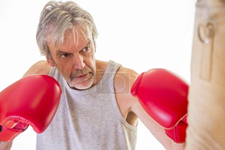 Photo for Senior man wearing gloves using a punching bag - Royalty Free Image