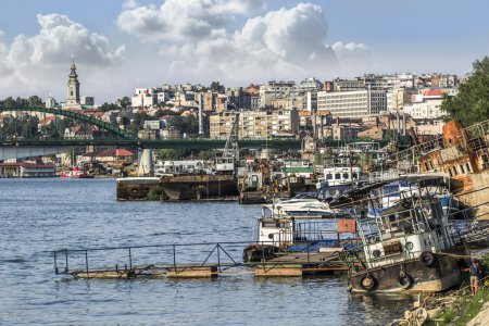 Téléchargez les photos : Belgrade, avec son clocher dominant de la cathédrale Saint-Michel, contraste avec les vieux bateaux et péniches abandonnés, rouillés, au premier plan, et le pont Old Sava au loin
. - en image libre de droit