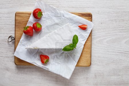 Photo for Brie uncovered on wooden plate on white table with strawberries - Royalty Free Image