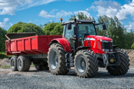 Photo for Red tractor with a trailer attached on gravel surface - Royalty Free Image