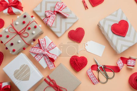 Valentine's Day composition with gifts and handmade hearts on beige background. Top view with blank tag for text.