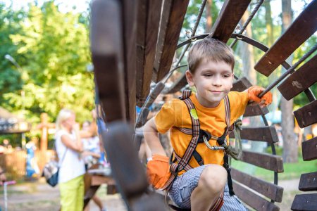 Niño feliz supera los obstáculos en el parque de aventura de cuerda. Concepto de vacaciones de verano. Niño jugando en el parque de aventuras de cuerda. Moderno parque de atracciones para niños. Juegos al aire libre