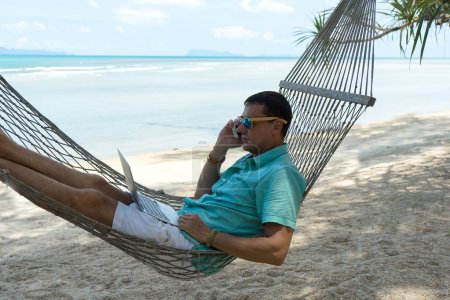 El hombre en los trópicos y con el ordenador Joven la belleza que yace en la hamaca con el portátil en el balneario tropical
