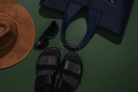 Sandalias de mujer, sombrero, bolso y gafas de sol sobre fondo verde. Accesorios de mujer. Vista superior