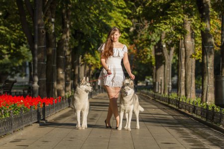 chica caminando por la calle con dos perros. Una chica con un vestido blanco. Huskies siberianos
.